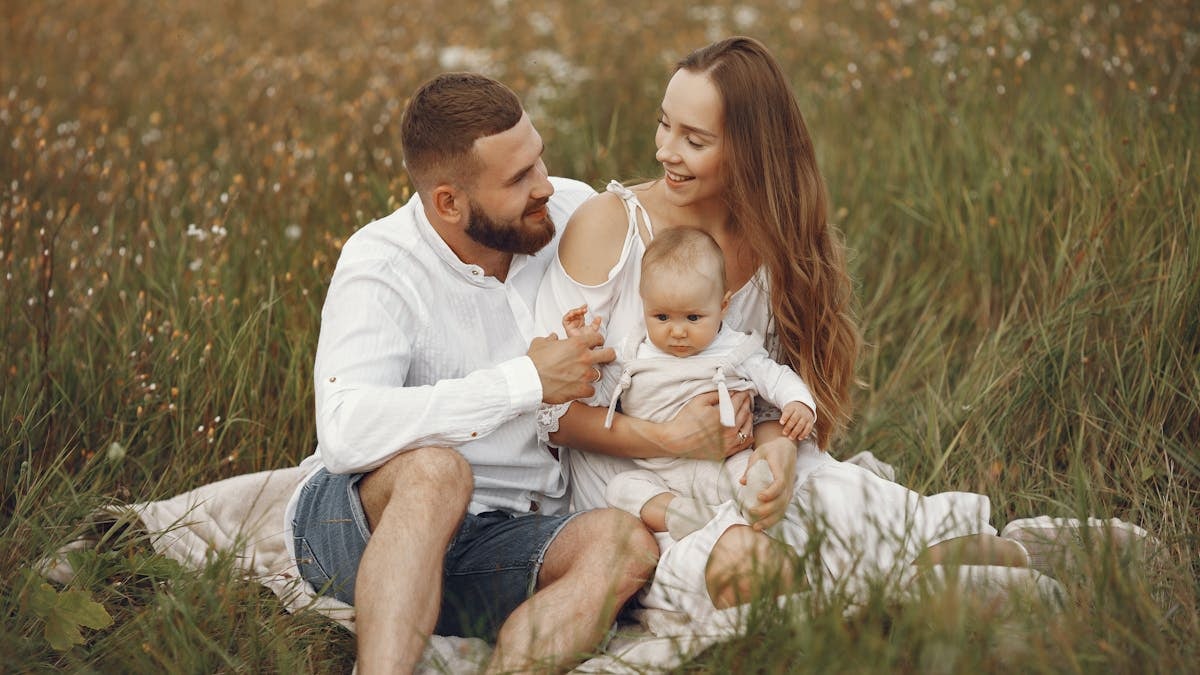 A joyful couple with their baby sitting on a blanket in a sunny meadow, embracing the beauty of summer.